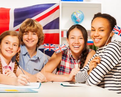 Four multiethnic teenage students sitting at the desk, holding British flags at the language courses
